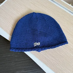 Nahaufnahme einer blauen Strickmütze im Detail mit feinem gestickten Buchstabenmotiv.