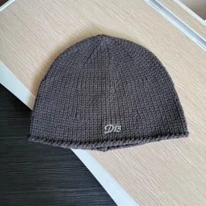 Dunkelgraue Strickmütze Detailaufnahme, mit gesticktem D13 Buchstaben für kalte Tage.