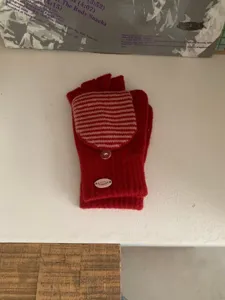 Primo piano di guanti in maglia rossa con patta a righe convertibile e dettaglio di bottone.
