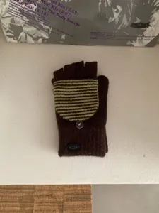 Primo piano di guanti convertibili in maglia marrone con patta a righe e bottone.