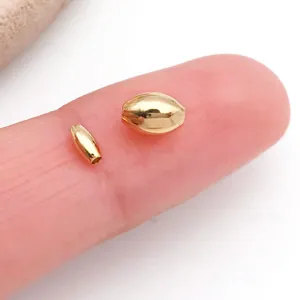 Detailed macro shot of small gold metallic spacer beads displayed on finger for size reference.
