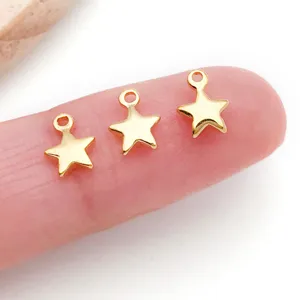 Primer plano detallado de tres mini dijes de estrella dorados en dedo para joyería DIY.