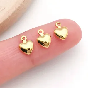 Primer plano de mini dijes de corazón chapados en oro en el dedo, ideales para joyería DIY.
