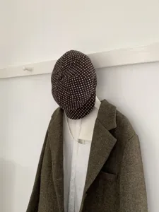 Braune gepunktete Schiebermütze kombiniert mit Tweed-Jacket und Spitzen-Oberteil Detail.