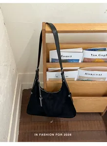 Gedetailleerd overzicht van een prachtige zwarte suède schoudertas op een houten rek.