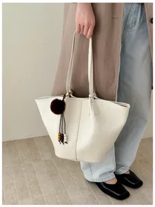 Close-up detail of white oil-wax leather tote bag with furry pendant charm in indoor setting.