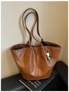 Detailopname van bruine PU-lederen tote bag met schouderbanden en leuke bedelhangers.