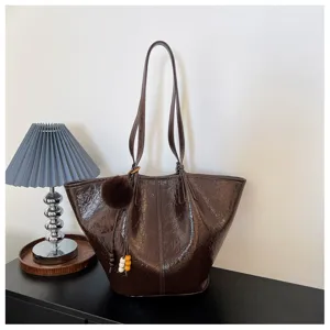 Dark brown oil wax leather tote bag detail, featuring long straps and fluffy pom-pom charm.