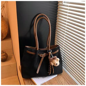 Zwarte suède shopper tas met bruine lederen handvatten, riemdecoratie en schattige berenhanger.