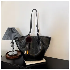 Close-up detail of the black oil wax leather tote bag featuring a fluffy pom-pom charm and sleek handle.