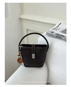 Détail de sac seau rétro, cuir sombre avec fermoir métallique et pendentif de perles.