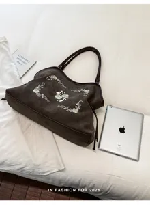 Gedetailleerd overzicht van een bruine suède handtas met elegante groene borduurdetails.