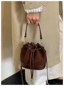 Detail van bruine suède bucketbag, trekkoordsluiting met goudkleurige hardware en lederen riem.