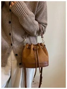 Detailopname van een bruine suède bucketbag met trekkoordsluiting en verstelbare schouderriem.