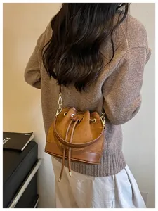 Gedetailleerd overzicht van de bruine suède bucketbag gedragen door model met leren afwerking.