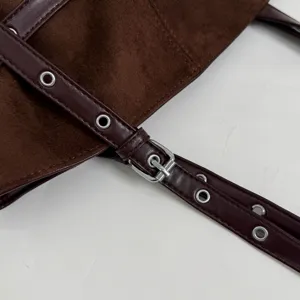 Close-up van een bruine lederen tassenriem met metalen oogjes en zilveren gespdetail.