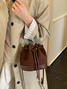 Elegante bruine suède emmertas met lederen afwerking, trekkoord en schouderriem.