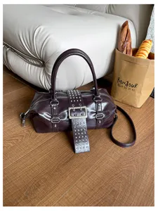 Detailopname van donkerpaarse Y2K Boston tas van leer met metalen studs en gespriem.