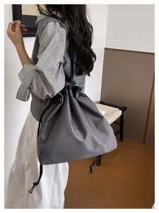 Detailaufnahme der grauen Nylon Kordelzug Umhängetasche am Model, lässiger Pendlerstil.