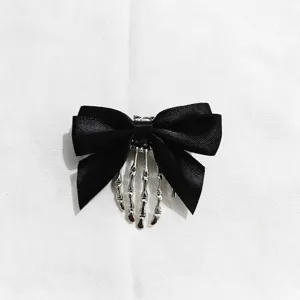 Detail shot of gothic black bow hairpin with silver skeleton hand charm, unique edgy accessory.