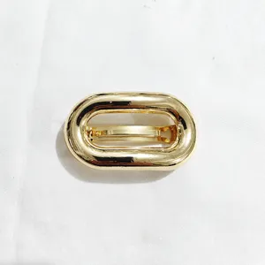 Dettaglio fermaglio capelli ovale in metallo dorato, molletta minimalista per styling quotidiano.