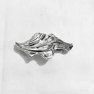 Close-up detail of silver liquid metal hair clip with unique wave design, shiny surface.