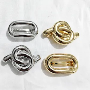 Primo piano di fermagli per capelli in metallo oro e argento con design ovali e intrecciati.