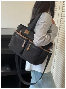 Gedetailleerd overzicht van de zwarte corduroy tote bag met meerdere zakken gedragen.