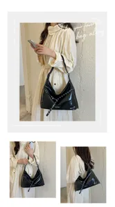 Black patent leather moto shoulder bag with metal eyelet details and adjustable buckle strap.