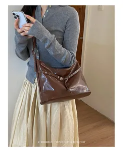 Retro brown patent leather shoulder bag with chic metal grommets and adjustable strap detail.
