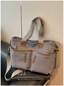Grijze corduroy tote tas met meerdere ritszakken en bruine lederen afwerking voor dagelijks gebruik.