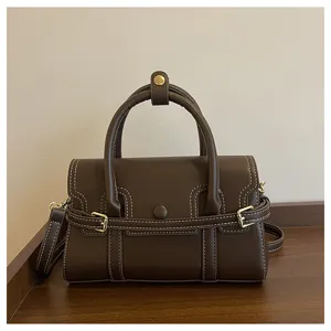 Donkerbruine retro leren handtas detailweergave met witte stiksels en luxe gouden gespen.