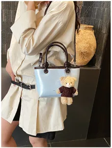 Detail shot of a stylish light blue tote bag with dark brown trim and cute teddy bear charm.