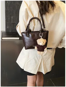 Detail view of a stylish dark brown PU leather tote handbag with a cute plush bear pendant.