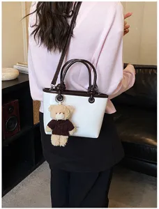 Detail view of the contrast tote bag with a cute plush bear pendant lifestyle shot.