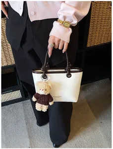 Handbag detail view showing contrast color design, leather texture, and cute teddy bear charm.