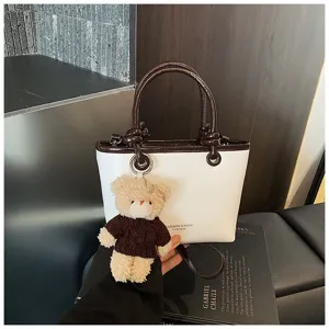Close-up detail of the white and brown color-block handbag with cute plush bear keychain.