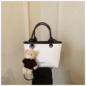 Close-up detail of stylish white contrast tote handbag with cute bear pendant charm.