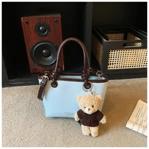 Light blue leather tote bag detail showing contrast brown trim and cute bear pendant charm.