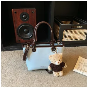 Detailed view of trendy contrast color tote bag with cute bear charm and brown trim.