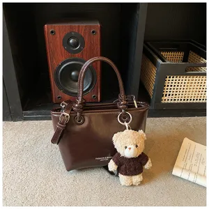 Detailed view of dark brown leather handbag featuring stylish handles and cute plush bear pendant.