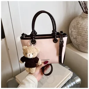 Detail shot of chic pink handbag with brown contrast trim and cute bear plush pendant.