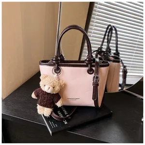 Pink colorblock detail view of fashionable leather crossbody handbag with cute bear charm.