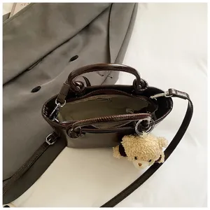 Dark brown leather handbag detail, featuring dual handles, shoulder strap and cute bear.