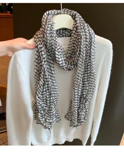 Detailansicht eines schwarz-weißen Schals mit Karomuster drapiert auf weißer Strickware.
