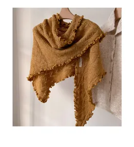 Vista detallada del chal triangular tejido en amarillo mostaza con bordes ondulados.