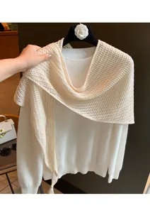Detail shot of solid color knit wool triangle shawl draped on sweater, stylish spring accessory.