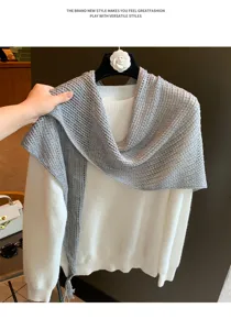 Detailed shot of a stylish grey knitted wool triangular scarf draped over a white sweater.