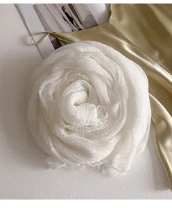 Nahaufnahme eines weißem knittrigen strukturierten Schals mit Quasten als Rosenblüte.