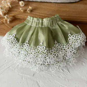 Détail en gros plan d'une jupe de poupée miniature en tissu vert avec dentelle.